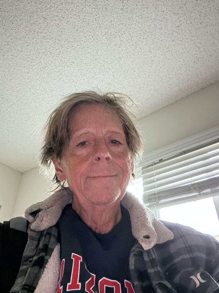 Middle-aged man with shoulder-length grayish hair wearing a dark shirt and sherpa-collared jacket indoors